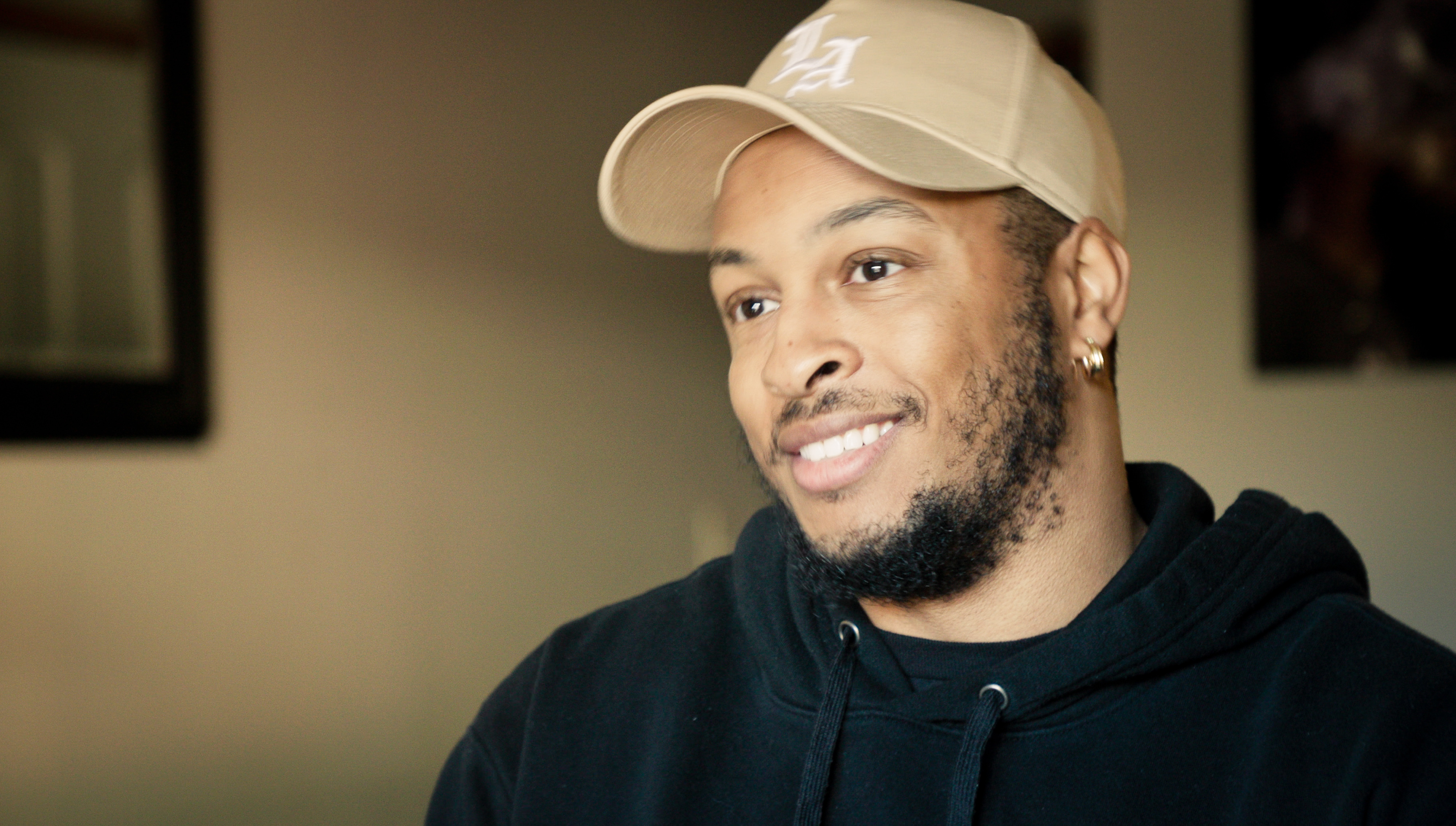 black male wearing a black shirt and tan cap smiling