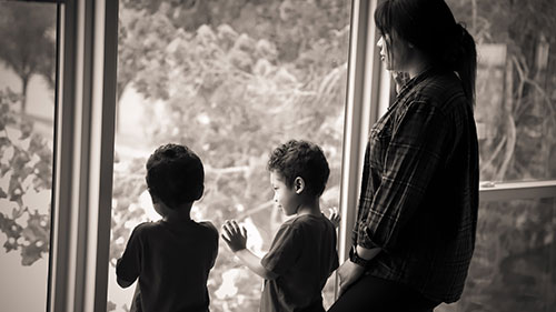 Woman and two young children looking out the window. One child has his hands on the glass.